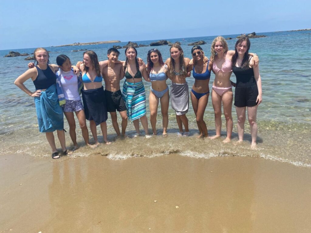 Group of students in bathing suits standing at the shoreline.