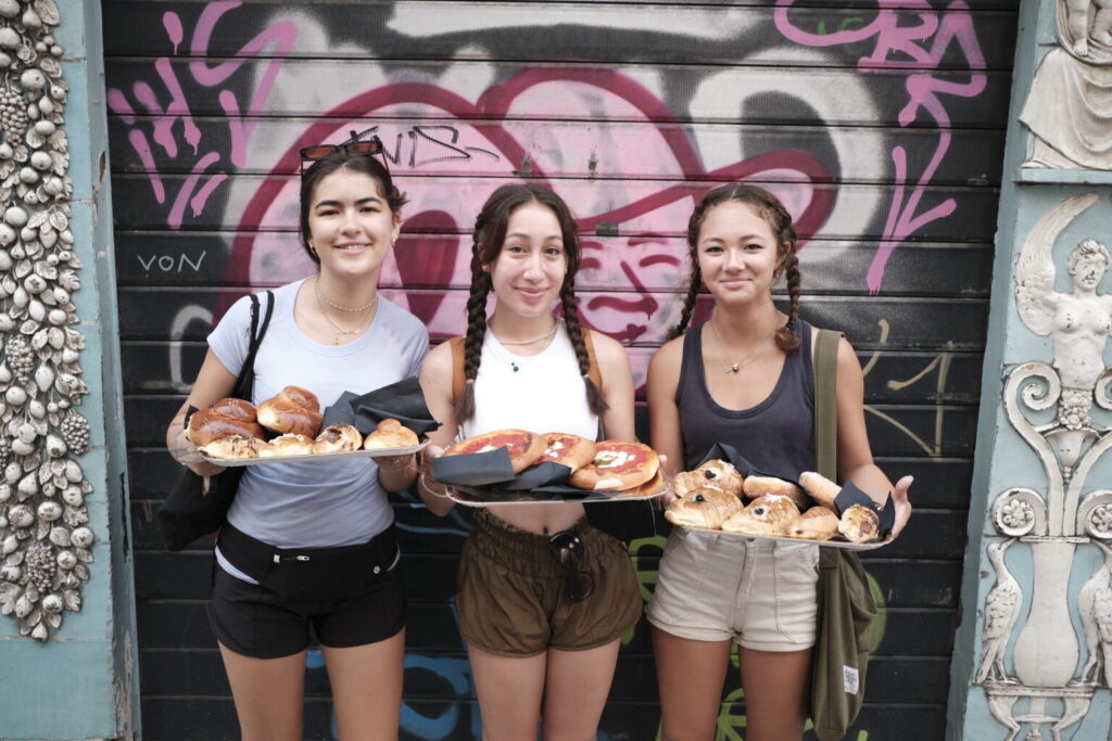 Three students holding trays of pastries.