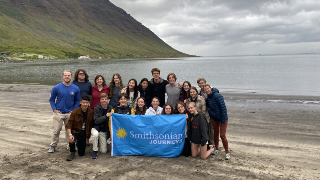 Group of students on beach holding blue Smithsonian Journeys flag.