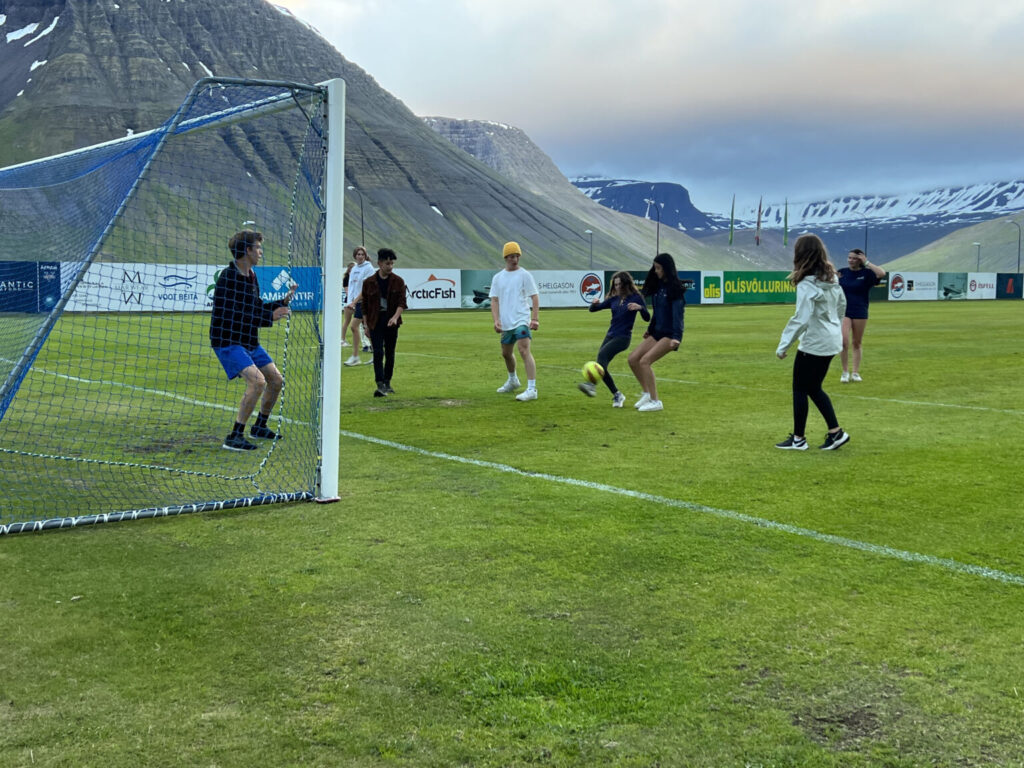 Students kicking soccer ball on green field.