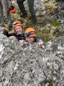 Two students in orange hard hats climbing rock.