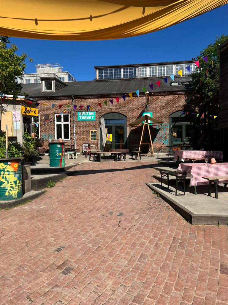 Outdoor brick patio with brick building and colorful flags hanging.