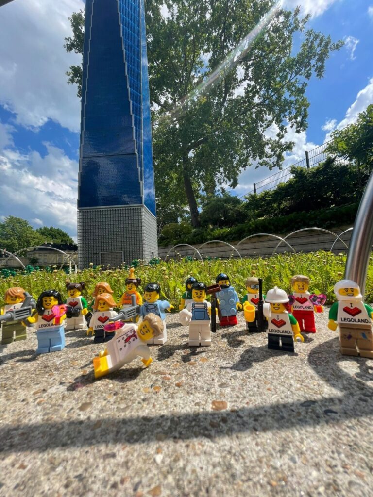 Close up photo of many little lego people figurines on the pavement in front of green grass.