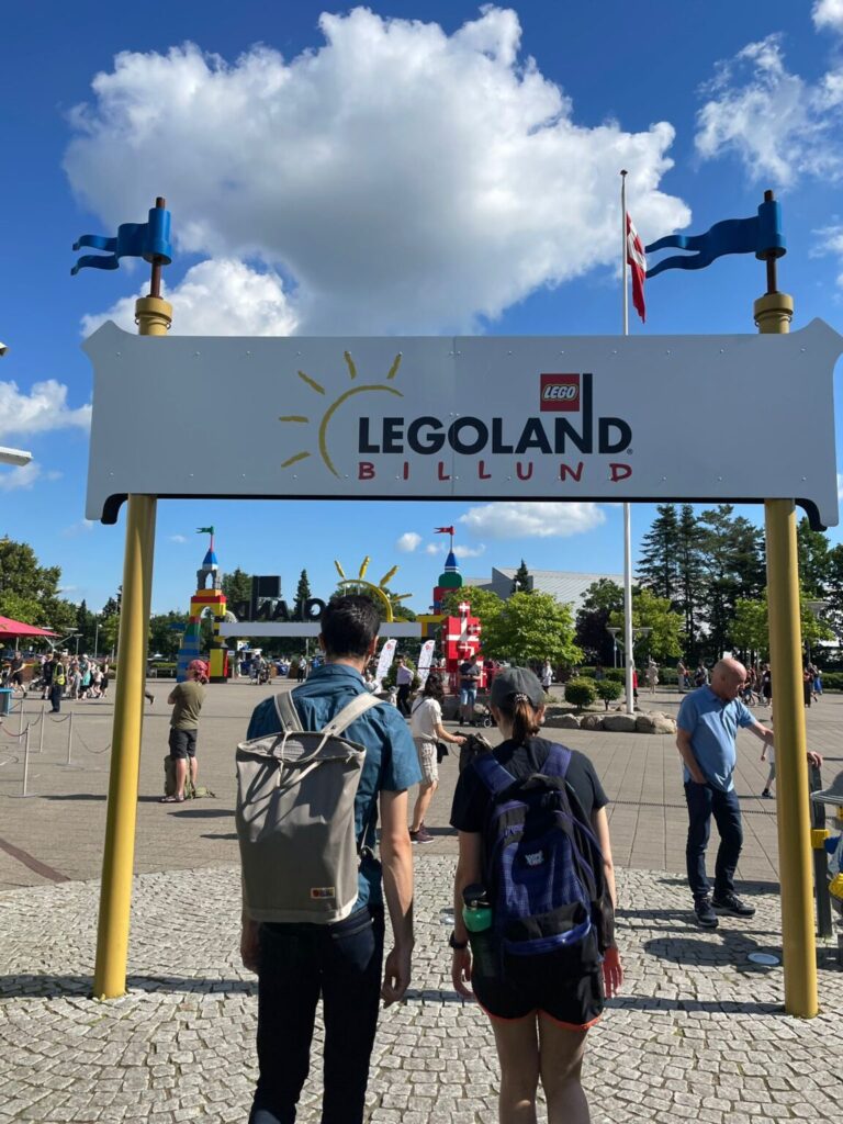 Two studnets with backpacks walking under Legoland Billund sign.