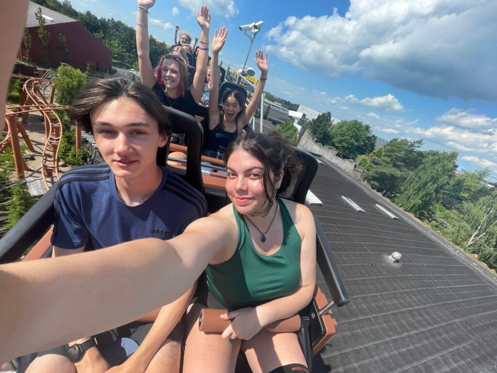 Girl taking selfie with other students on a rollercoaster.