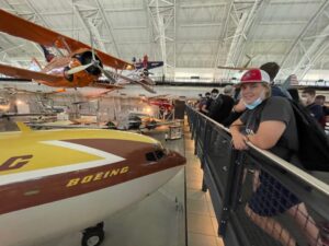 Student smiling next to front of old yellow and brown Boeing plane.