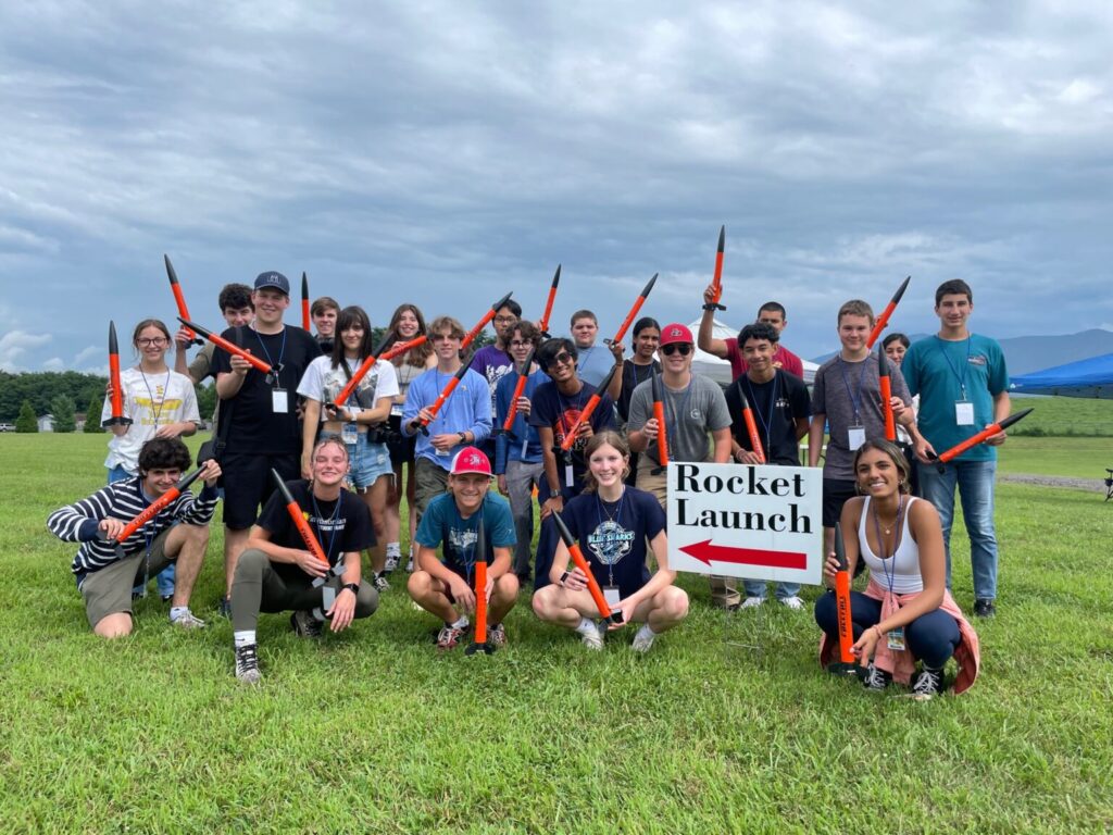 Group of students holding sign that reads "Rocket Launch" with a red arrow pointing left.