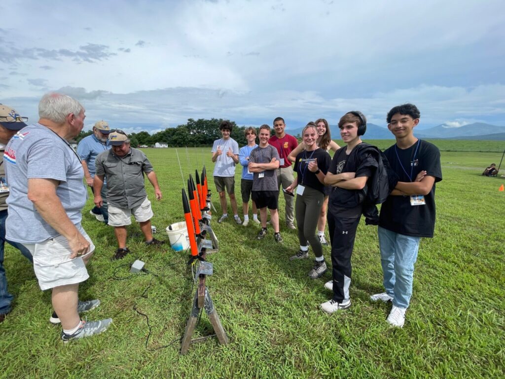 Students standing in front of small orange rockets.