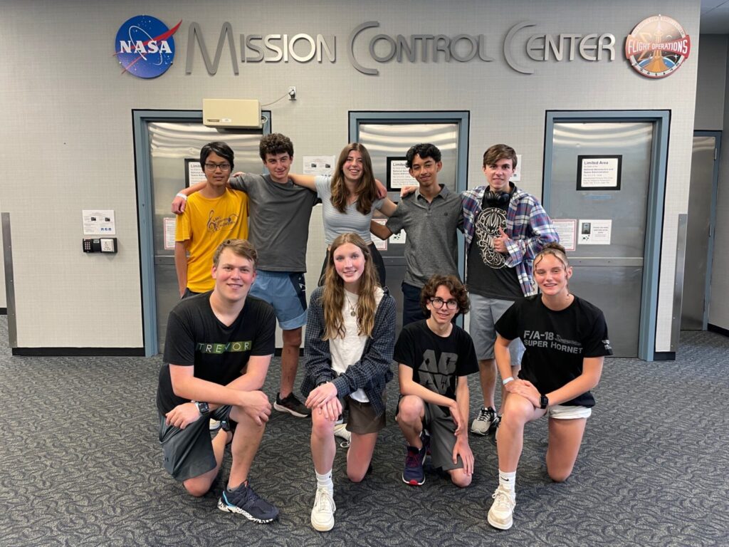 Nine students smiling in front of Nasa Mission Control Center sign.