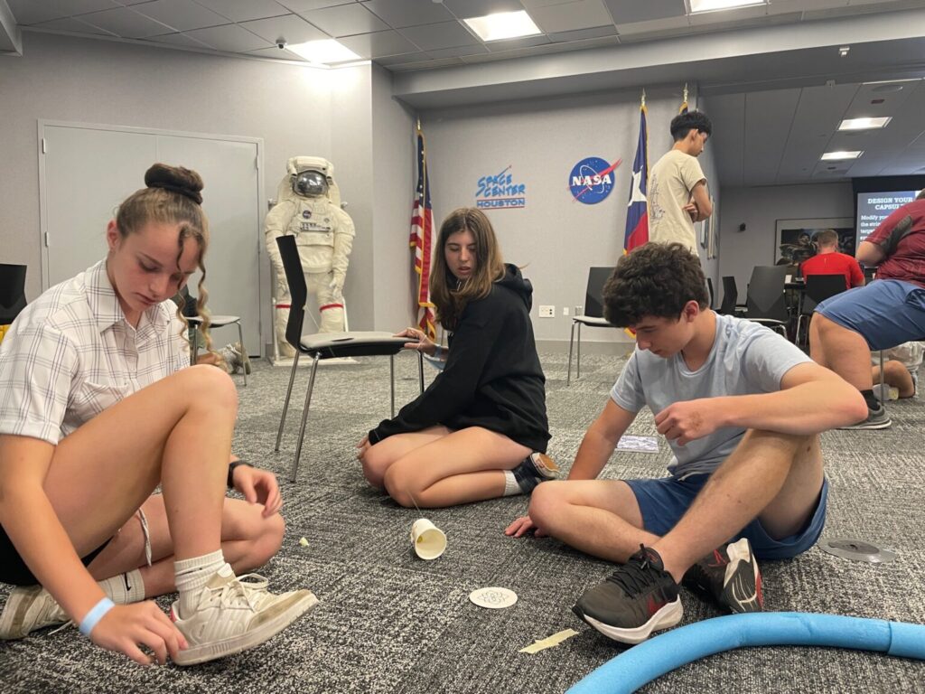 Three students sitting on ground working on project.