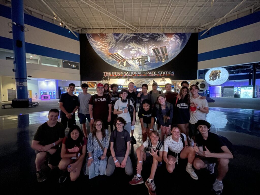 Large group of students smiling together in front of The International Space Station banner.