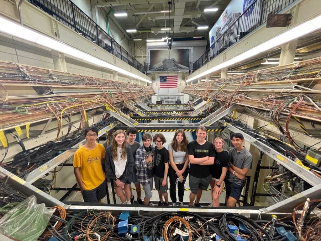 Nine students smiling standing in front of the Ghost Shuttle.